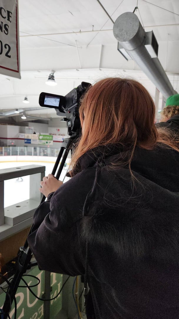 student operating a camera at a hockey game