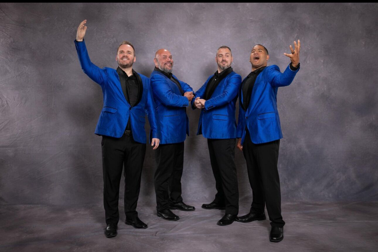 Group of four students dressed in blue blazers, posing for the camera